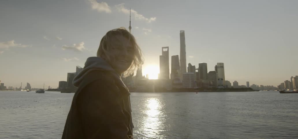 A woman looking out at some water and buildings while standing next to a rail