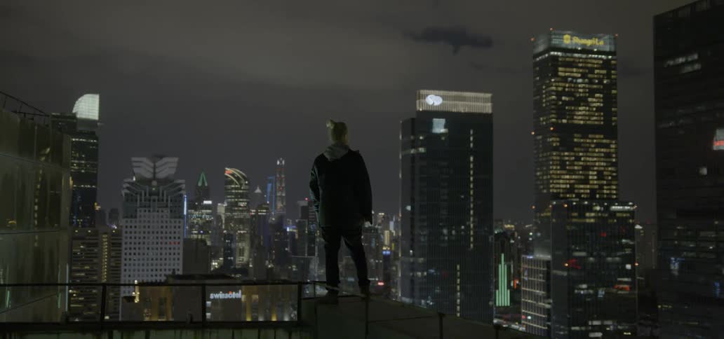 A person standing on a rail on top of a building looking at other buildings