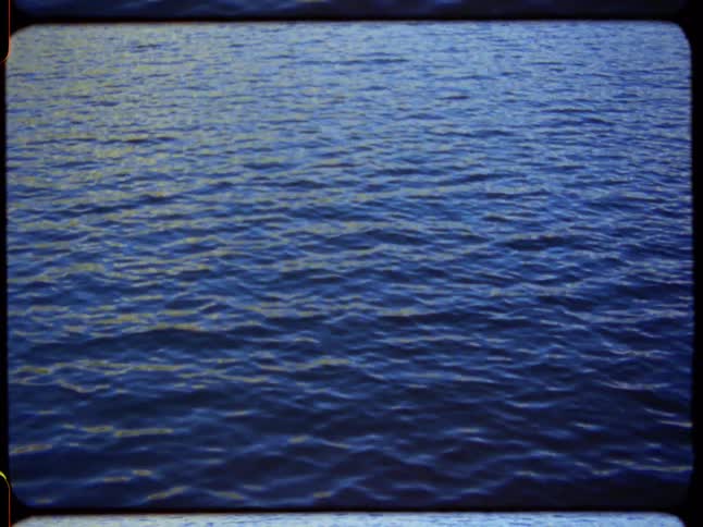 A serene, static shot captures the hypnotic ripples on the surface of deep blue water with a vintage film effect