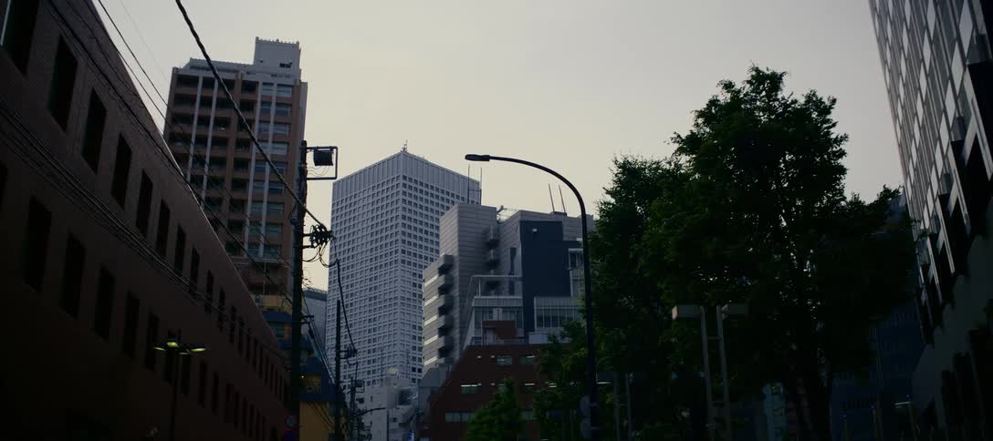 A slow cinematic zoom reveals the towering skyscrapers of a modern Japanese city street on an overcast day