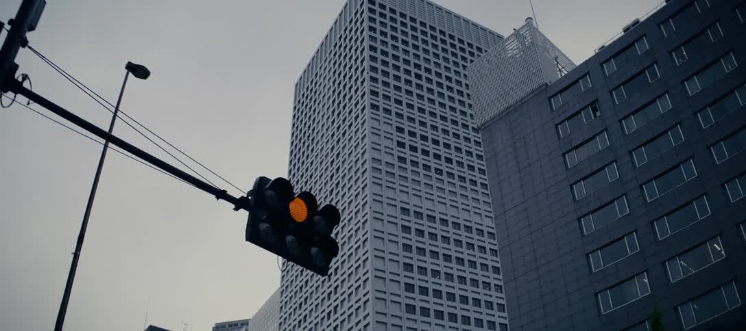A low angle shot shows a traffic light cycling through its colors with imposing city skyscrapers in the background