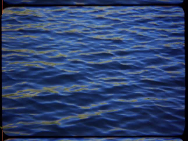 A vintage, Super 8 film style shot focuses on the mesmerizing ripples of deep blue water with golden reflections