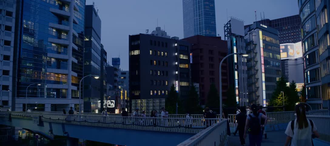 A slow-motion shot of people walking across a bridge in a bustling Tokyo neighborhood at dusk