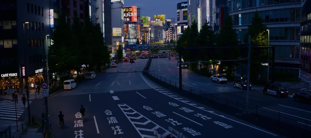An evening view of a major Tokyo intersection with bustling traffic and pedestrians under the glow of vibrant city billboards