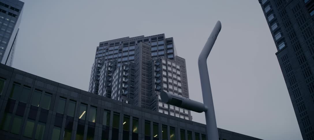 A low-angle tracking shot of a modern architectural skyscraper against a stark, overcast sky