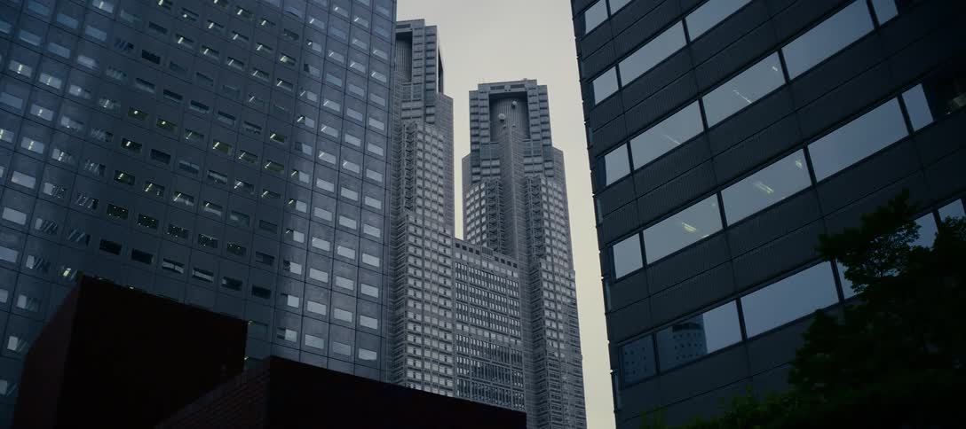 A low-angle shot of the Tokyo Metropolitan Government Building slowly tilts down, revealing the surrounding modern architecture and trees