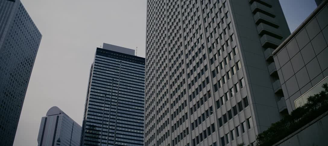 A slow dolly shot past the imposing concrete and glass facades of modern skyscrapers on an overcast day