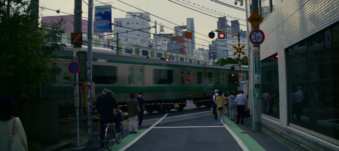 A classic Tokyo city scene captures pedestrians waiting at a railway crossing as one train speeds by on the tracks and another passes on an overpass above