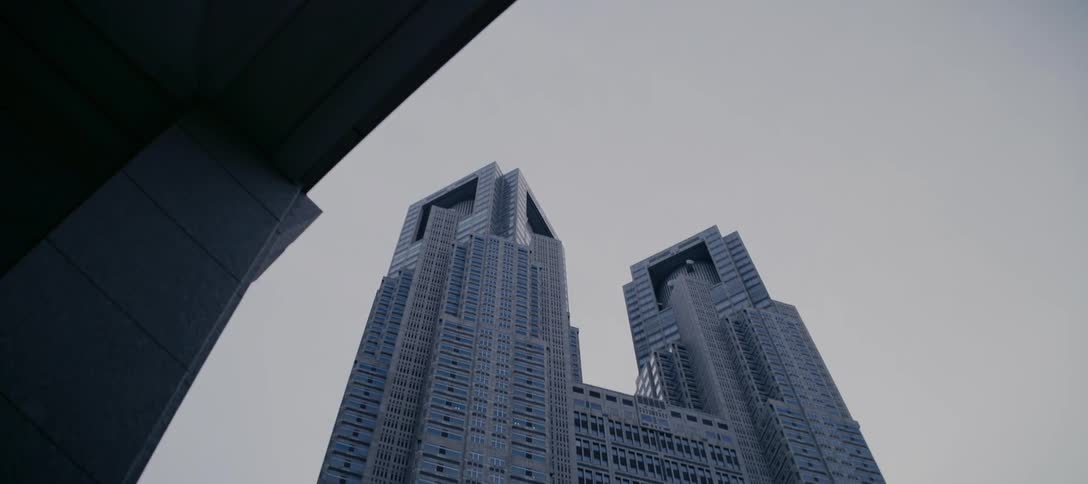 A slow, low-angle reveal shot of the impressive Tokyo Metropolitan Government Building against an overcast sky