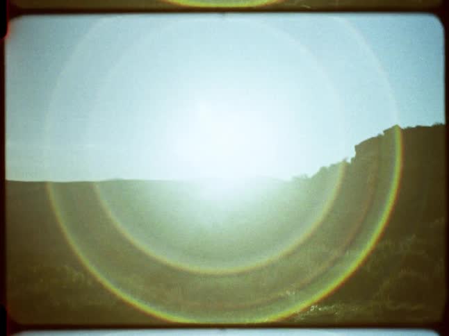 A dreamy, vintage-style shot of the sun rising over a hazy, hilly landscape, creating a beautiful rainbow lens flare