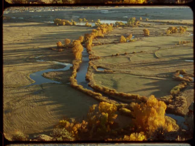 A vintage, high-angle shot captures a meandering river winding through a vast valley with golden autumn foliage at sunset