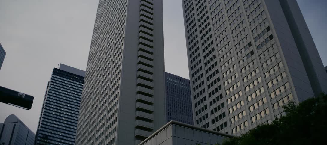 A slow tilt reveals the towering modern skyscrapers of a city's financial district under an overcast sky