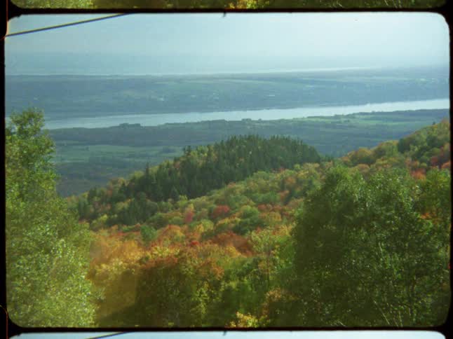 A scenic overlook from vintage film shows a river valley with rolling hills covered in vibrant autumn foliage