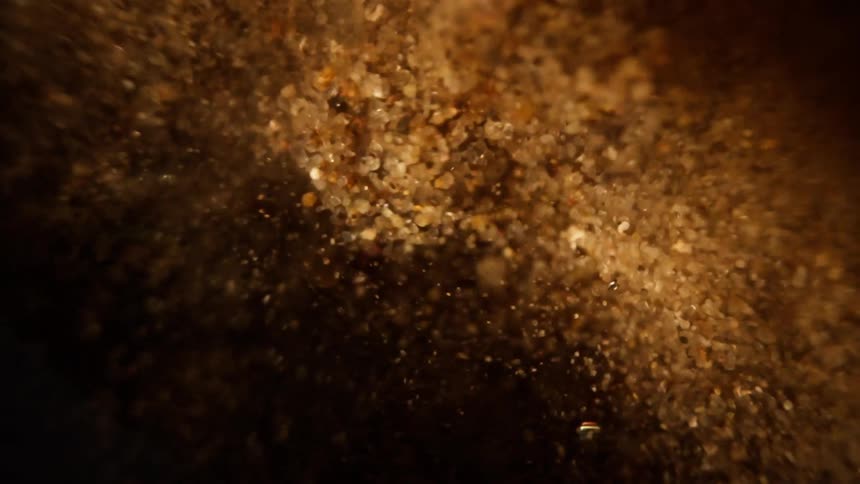 A mesmerizing close-up of golden sand particles slowly floating and twisting in a dark liquid