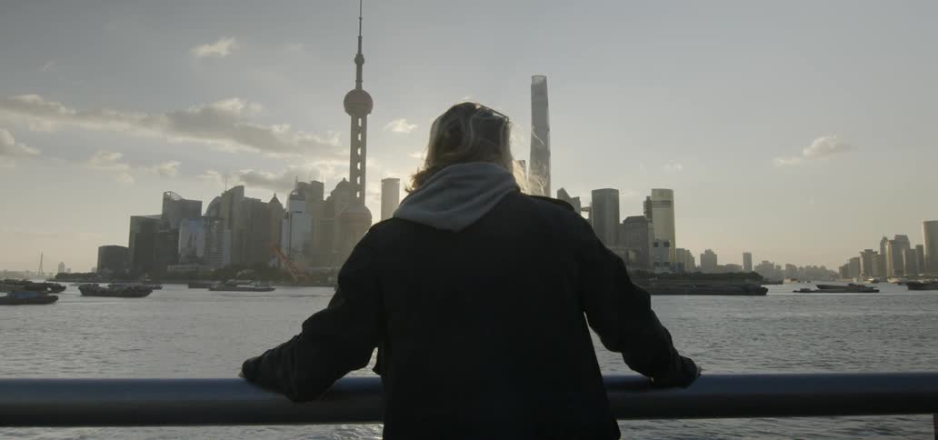 A man is walking toward a railing to view a city and harbor