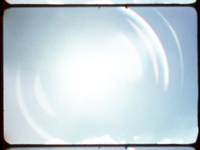 Vintage film footage with a lens flare transition reveals a serene view of an empty chairlift over a snowy mountain