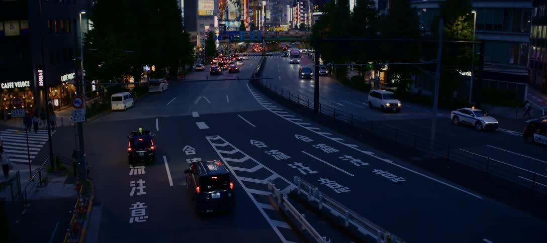 A slow high-angle zoom out reveals a busy street in Tokyo with traffic flowing under the bright city lights at dusk