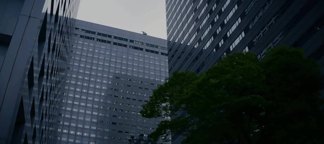 A slow-moving shot looks up at imposing modern skyscrapers in a dense urban business district under an overcast sky