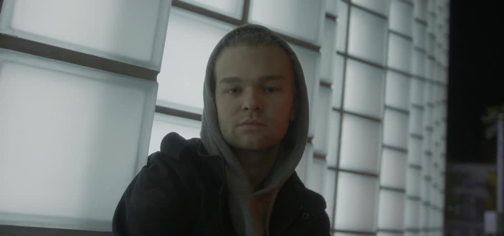 A man looks up slowly leaning against a wall
