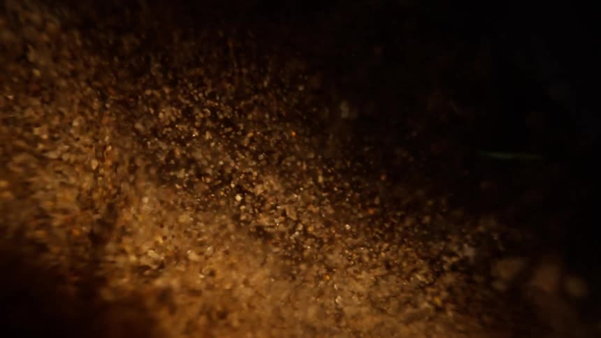 A macro close-up of warm, golden sand particles slowly flowing downwards against a dark background