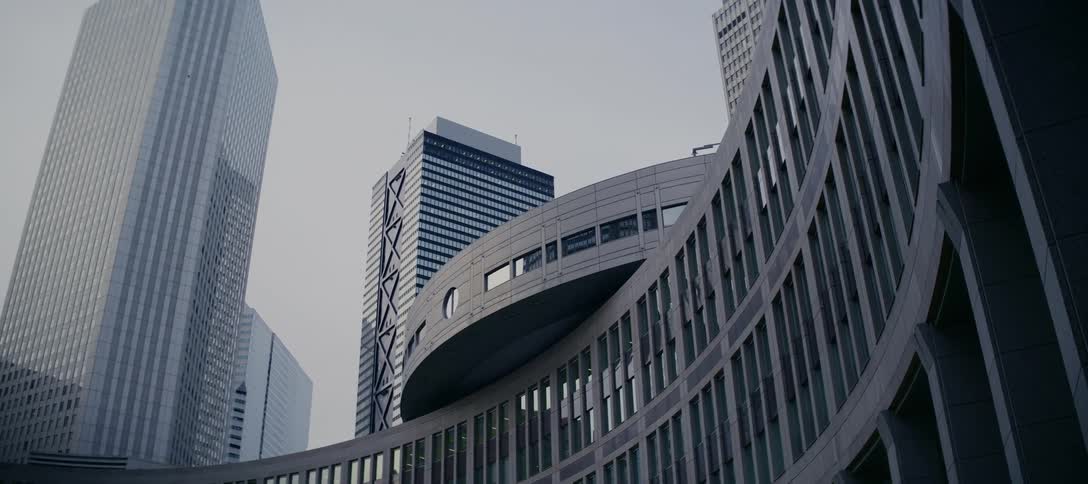 A slow tracking shot past a tree reveals the unique curved architecture of modern skyscrapers in a futuristic cityscape