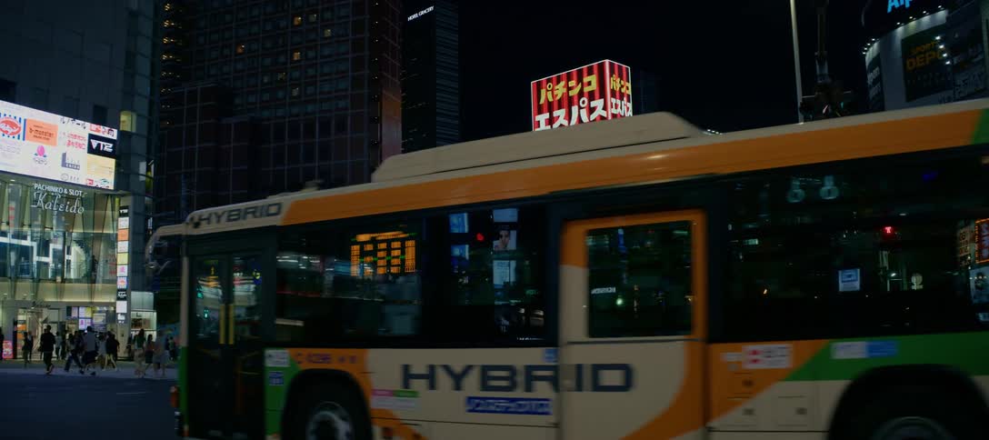 Slow-motion shot of a bustling Tokyo crosswalk at night as pedestrians and traffic navigate the vibrant city streets