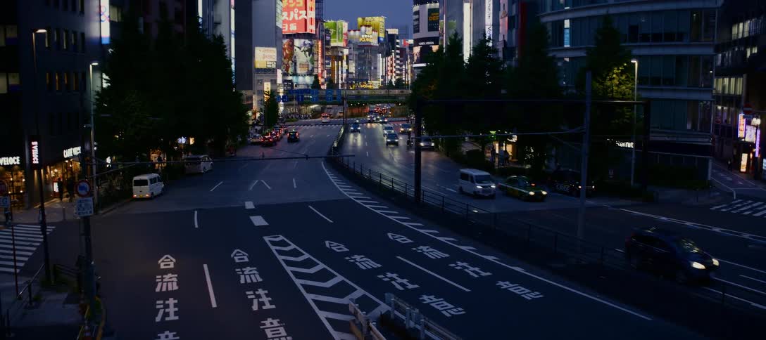 High-angle view zooms out from Japanese road markings to reveal a bustling city street in Tokyo at dusk with cars and illuminated billboards