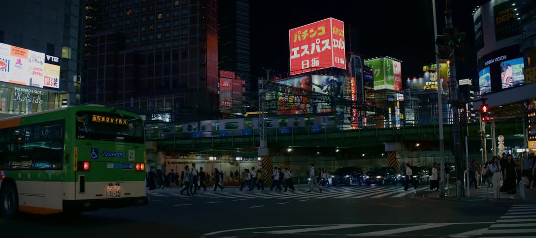 An elevated train passes over a bustling crosswalk in a vibrant Japanese city at night, surrounded by towering buildings and neon signs