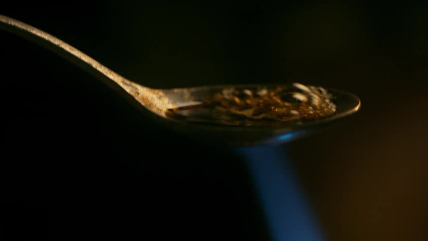A macro shot shows a drug being heated and boiled in a spoon with a lighter