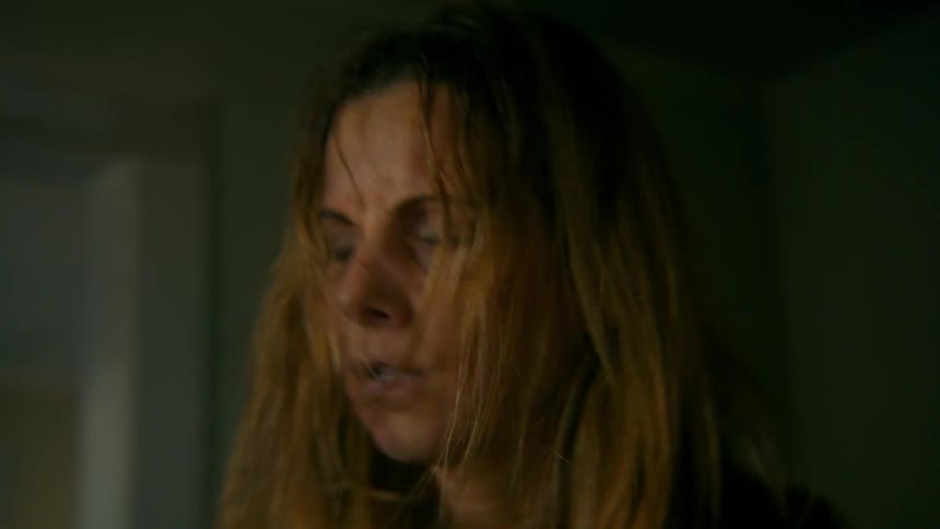 A close-up slow-motion shot reveals a terrified and injured woman with cuts and bruises on her face looking around nervously