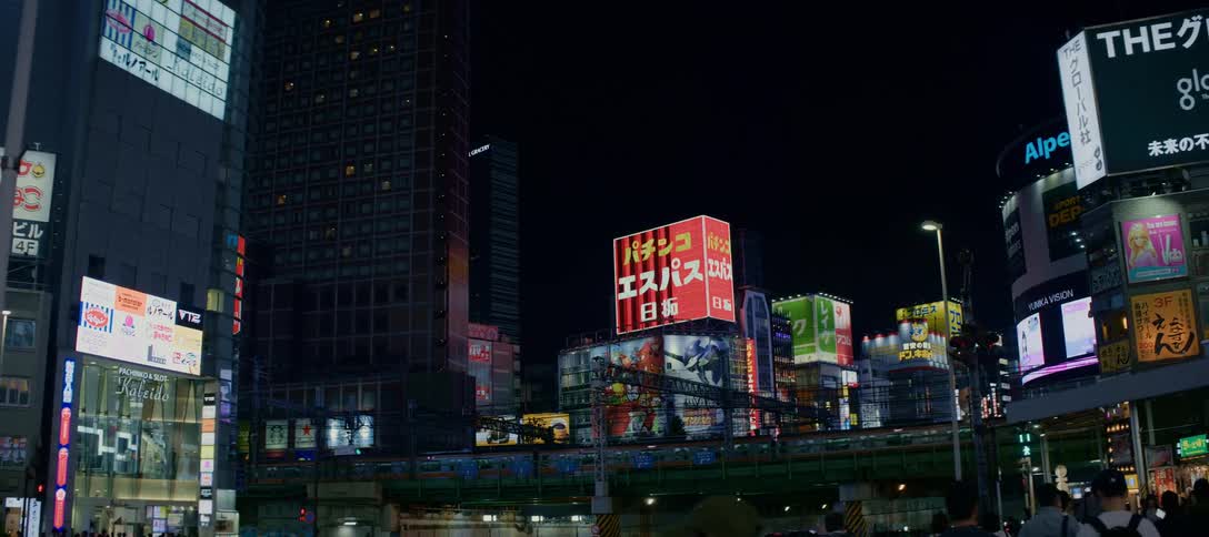 A busy Tokyo street comes alive at night with vibrant neon signs as a train passes over an elevated track above the bustling traffic