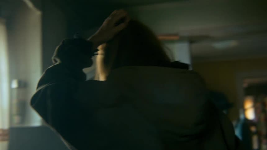 A distraught and disoriented woman stumbles through a dark, cluttered, and abandoned house