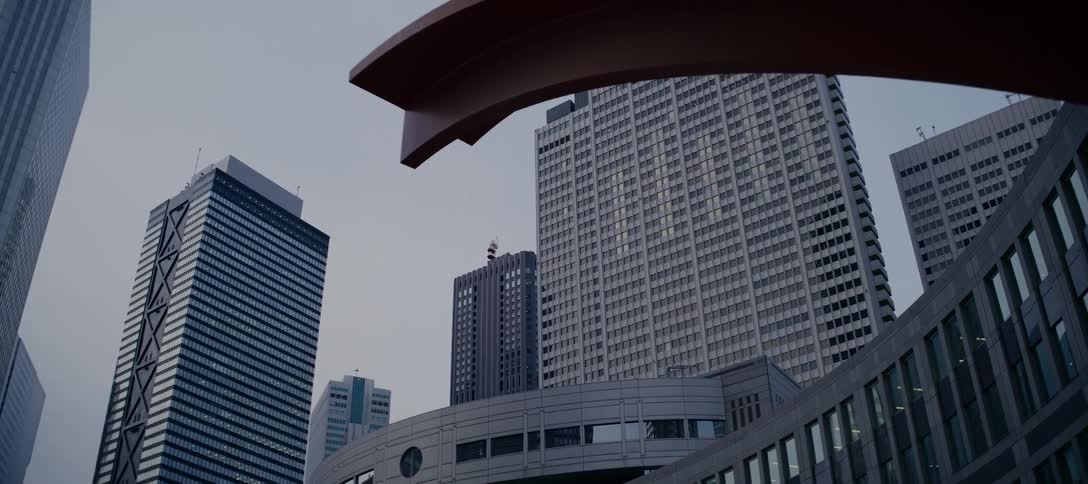 A low-angle tracking shot slowly pulls back to reveal the impressive modern skyscrapers of Tokyo's financial district on an overcast day