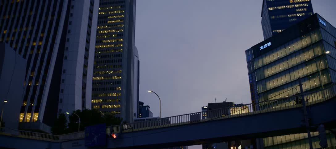 A slow camera pan tilts up from a city street at dusk to reveal the illuminated skyscrapers of a modern Japanese city