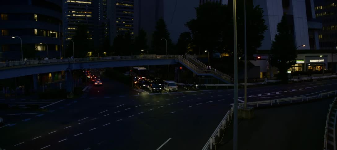 A slow tilt down from towering skyscrapers reveals a street-level view of city traffic at an intersection in Tokyo at night