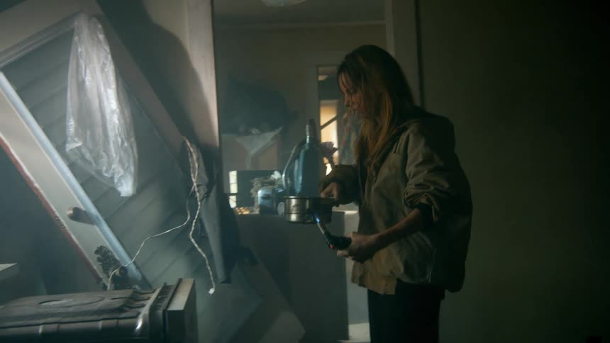 A determined woman uses a blowtorch to cook a meal in a pot while surviving in a dark and derelict house