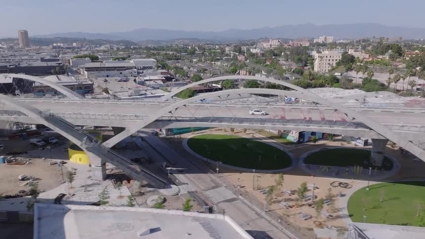An aerial view pans across the iconic Sixth Street Viaduct in Los Angeles, showing traffic flowing over its modern arches on a sunny day