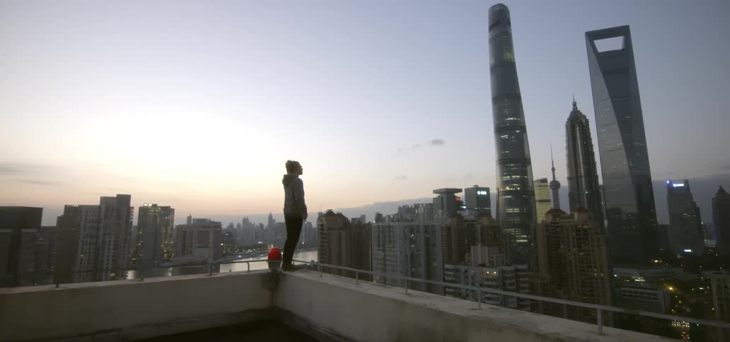 A man stands on a roof viewing a city