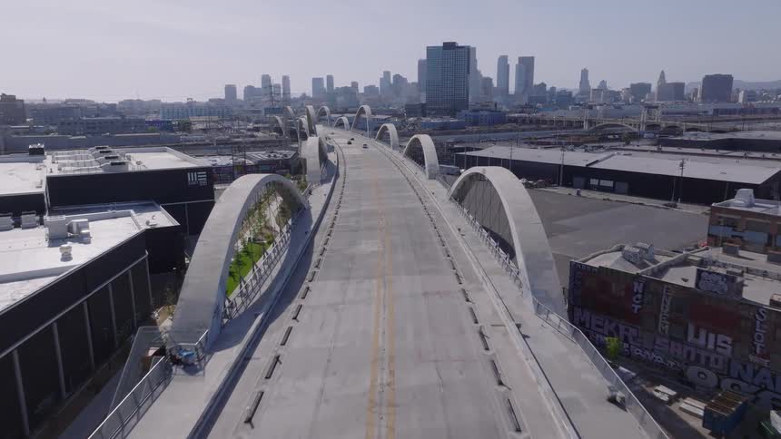 An aerial view slowly flying over the iconic 6th Street Viaduct bridge towards the downtown Los Angeles skyline on a clear day
