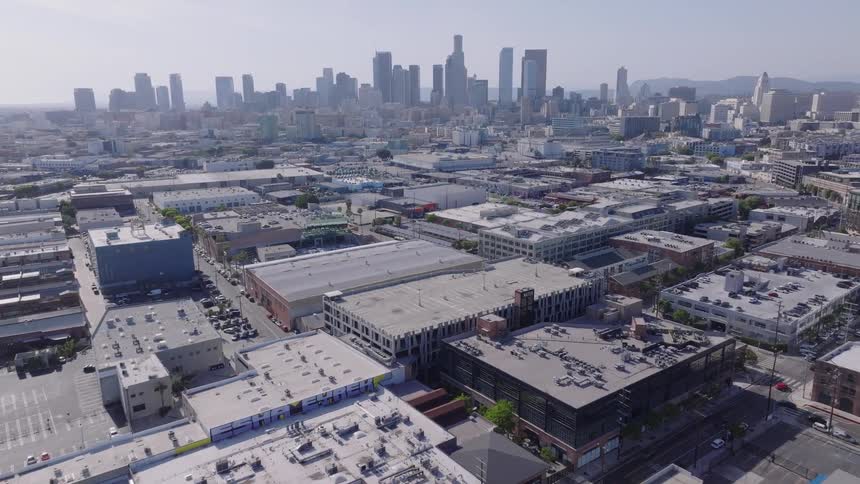 Aerial view slowly flying over the industrial arts district toward the downtown Los Angeles skyline on a clear, sunny day
