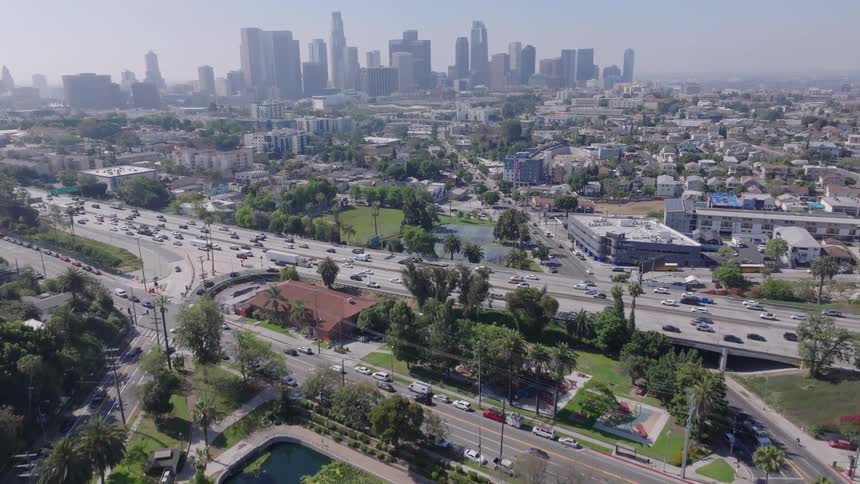 An aerial view begins over Echo Park Lake before ascending to show the bustling Hollywood Freeway and the downtown Los Angeles skyline