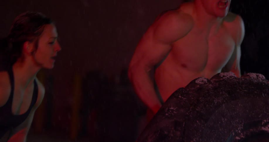 A female athlete is encouraging a male athlete to lift a large tire