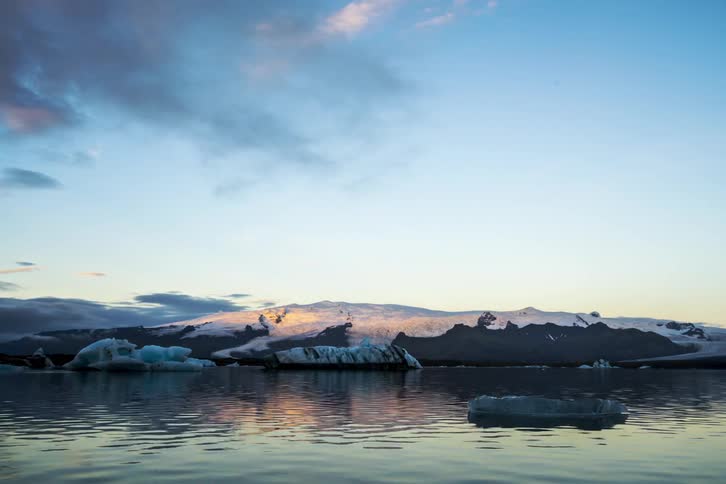 A block of ice floats past a mountain shoreline