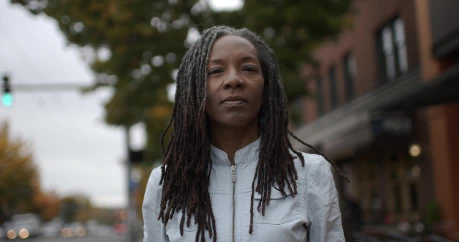 A woman with dreadlocks looking at the camera while outside in front of a building