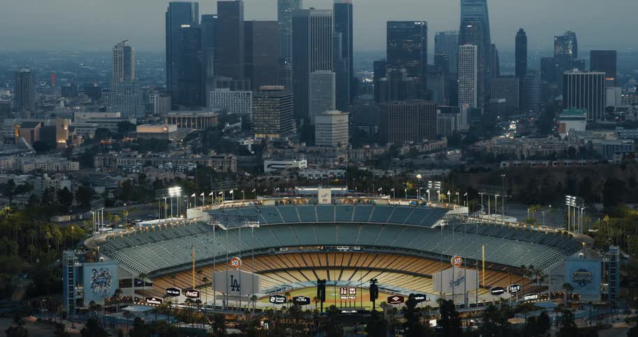 Stunning aerial view of a lit-up Dodger Stadium at dusk with the downtown Los Angeles skyline in the background