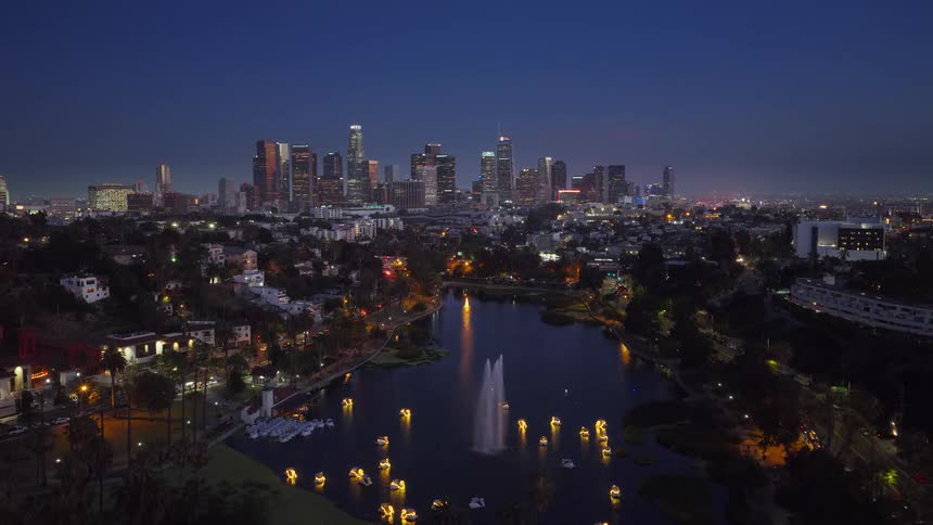 An aerial view of the Los Angeles skyline at night over Echo Park Lake with its illuminated fountain and swan paddle boats