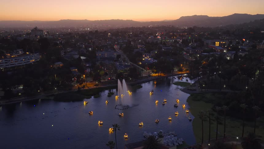 Aerial view of Echo Park Lake in Los Angeles at dusk, with illuminated swan boats gathered around a large central fountain
