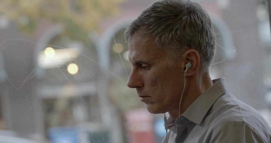 A man is sitting by a window wearing earplugs