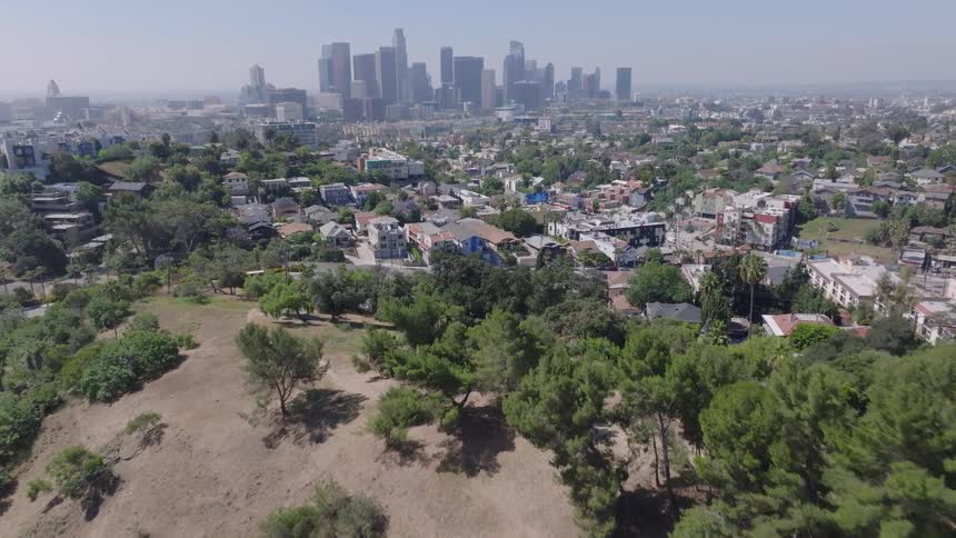 Aerial view flying over a park and residential neighborhood towards the downtown Los Angeles skyline on a clear sunny day