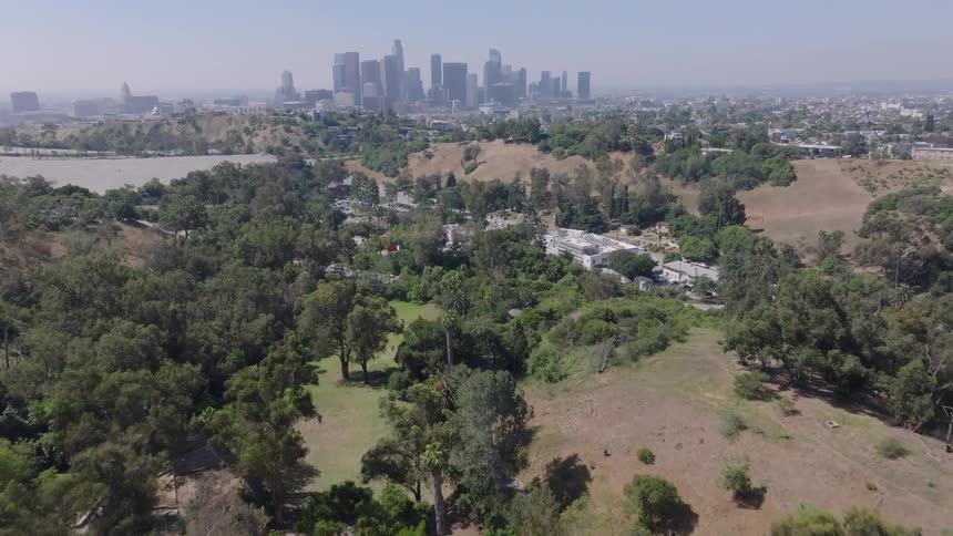 An aerial view flies over Elysian Park with the Downtown Los Angeles skyline in the background on a sunny day